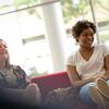 Two students sit next to each other on a couch, engaged in a group discussion.