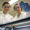 Two students in lab coats performing research in a lab
